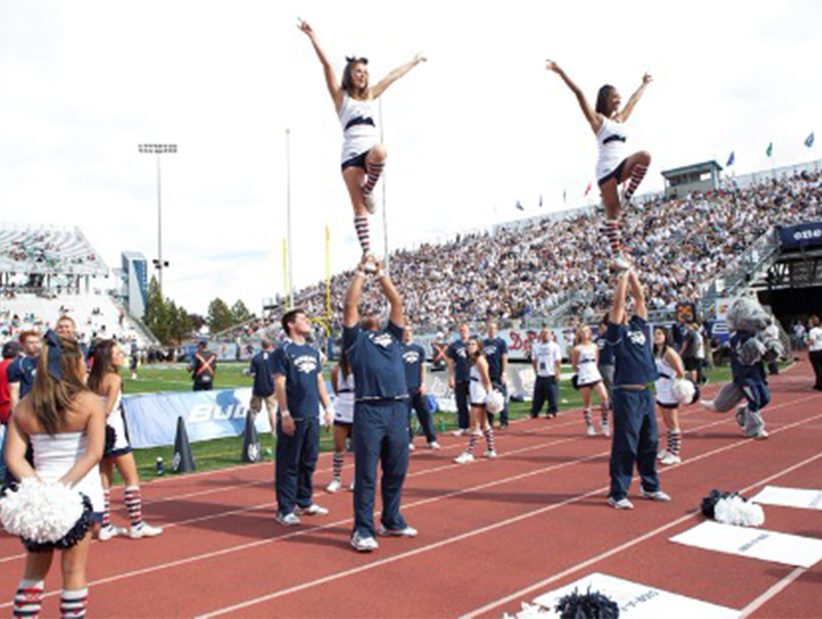 Two University of Nevada, Reno cheerleaders are balanced in the air as a roaring football crowd looks on.